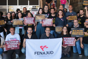 Imagem Acessível: Grupo de pessoas com cartazes de protesto contra o Regime de Recuperação Fiscal (RRF), duas pessoas em primeiro plano exibem a bandeira da Fenajud. Estão presentes os diretores do Serjusmig e do SINJUS-MG. Representando o SINJUS estão Alexandre Pires, coordenador-geral, Felipe Rodrigues, Alexandre Pires, Janaína Torres e o servidor Wagner Ferreira. Conteúdo textual: ALTERNATIVAS À VISTA - STF prorroga prazo da dívida e votação do RRF é adiada novamente