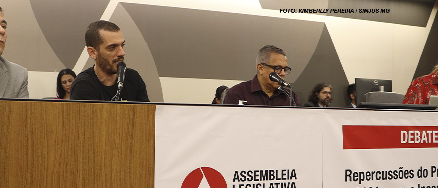 A imagem mostra uma cena de debate público realizado na Assembleia Legislativa de Minas Gerais, onde o coordenador-geral do SINJUS, Alexandre Pires, participa de uma discussão contra o desmonte do Ipsemg. Na parte superior há pessoas sentadas, com microfones, em um ambiente de debate formal