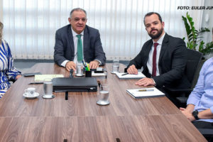 A imagem mostra uma reunião em uma sala de conferências, onde há dois representantes da administração do TJMG e dois diretores do SINJUS sentados ao redor de uma mesa de madeira. Ao fundo, é possível ver janelas com persianas fechadas e algumas plantas ornamentais. Estão presentes à mesa o 1º vice-presidente do TJMG, desembargador Marcos Lincoln, Alexandre Pires (coordenador-geral do SINJUS-MG) e Felipe Rodrigues (diretor de Assuntos Jurídicos).