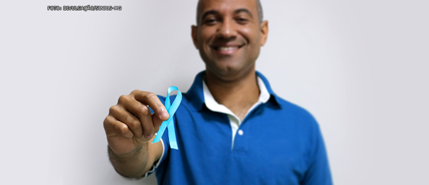 #ImagemAcessível Diretor do SINJUS Wagner Ferreira sorrindo e segurando à frente um laço azul (homem negro, cabelo curtos e vestindo uma camisa também azul).