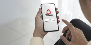 A imagem mostra uma pessoa segurando um smartphone, onde aparece a tela inicial do aplicativo da carteira funcional digital do Tribunal de Justiça de Minas Gerais (TJMG). O logo do TJMG está destacado na tela do celular. A cena tem um tom profissional e minimalista, com o fundo desfocado, dando ênfase ao telefone.