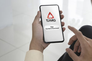 A imagem mostra uma pessoa segurando um smartphone, onde aparece a tela inicial do aplicativo da carteira funcional digital do Tribunal de Justiça de Minas Gerais (TJMG). O logo do TJMG está destacado na tela do celular. A cena tem um tom profissional e minimalista, com o fundo desfocado, dando ênfase ao telefone.