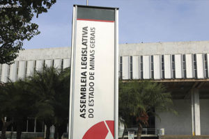 Fotografia diurna da fachada da Assembleia Legislativa de Minas Gerais (ALMG) com foco na placa vertical da mesma.