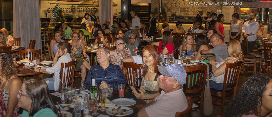 As imagens mostram um evento de confraternização em um restaurante, com diversas pessoas sentadas em mesas, conversando e aproveitando um momento de integração. As mesas estão repletas de pratos e copos. O ambiente é aconchegante, com iluminação interna e uma decoração acolhedora. Em uma das fotos, algumas pessoas estão em pé diante de um banner decorativo, realizando um discurso ou apresentação. A atmosfera geral sugere um encontro descontraído e amigável, reforçando os laços entre os servidores do NAP e NPD.