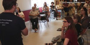 A imagem mostra um grupo de pessoas em uma sala de aula ou reunião, onde o NAP discute os benefícios da atividade física para pessoas com mais de 50 anos. Vários participantes estão sentados, atentos, enquanto um palestrante com microfone apresenta o conteúdo, todos engajados e interessados no tema. Em uma imagem adicional, vemos um grupo de pessoas, incluindo instrutores e participantes, posando sorridentes.