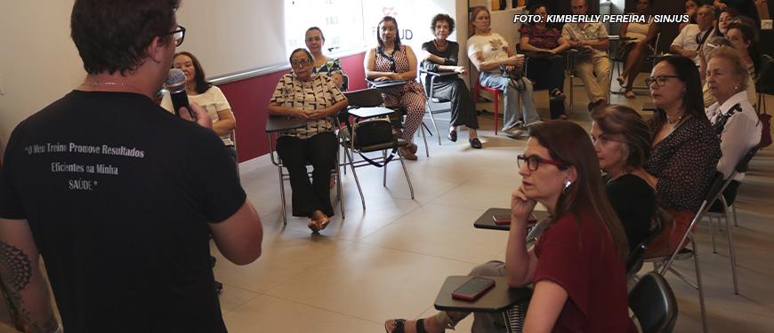 A imagem mostra um grupo de pessoas em uma sala de aula ou reunião, onde o NAP discute os benefícios da atividade física para pessoas com mais de 50 anos. Vários participantes estão sentados, atentos, enquanto um palestrante com microfone apresenta o conteúdo, todos engajados e interessados no tema. Em uma imagem adicional, vemos um grupo de pessoas, incluindo instrutores e participantes, posando sorridentes.