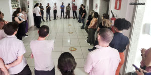 Na foto, observamos uma reunião setorial do SINJUS-MG na unidade Praça Milton Campos do TJMG. Os servidores estão dispostos em círculo em um corredor amplo, demonstrando engajamento coletivo. Eles escutam atentamente as orientações e discussões promovidas por membros da diretoria do sindicato, que se encontram ao fundo, coordenando a conversa.