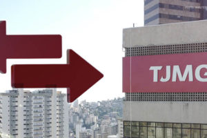 A imagem mostra o prédio do Tribunal de Justiça de Minas Gerais (TJMG), com a sigla TJMG exibida em grande destaque na fachada. Há também duas setas vermelhas apontando em direções opostas simbolizando o conceito de "remoção" , sobrepostas na parte esquerda da imagem. Ao fundo, é possível ver uma vista da cidade com vários prédios e o céu claro.