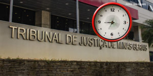 Fachada do Tribunal de Justiça de Minas Gerais (TJMG), com letreiro em destaque na parte inferior da imagem. Acima do prédio, há um relógio digitalmente inserido na imagem, com moldura vermelha e ponteiros marcando aproximadamente 9h05. No canto superior direito, há um crédito de imagem com o texto