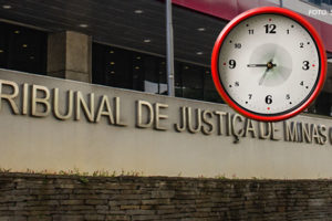 Fachada do Tribunal de Justiça de Minas Gerais (TJMG), com letreiro em destaque na parte inferior da imagem. Acima do prédio, há um relógio digitalmente inserido na imagem, com moldura vermelha e ponteiros marcando aproximadamente 9h05. No canto superior direito, há um crédito de imagem com o texto