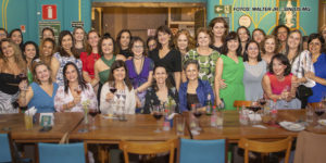 As imagens mostram a confraternização do Núcleo das Mulheres, onde um grupo diverso de mulheres celebra um ciclo em um restaurante, sentadas em mesas compridas e alegres, segurando taças de vinho. Elas aparecem bem arrumadas, sorrindo e interagindo entre si. O ambiente tem uma decoração acolhedora e vibrante, com detalhes coloridos nas paredes. A atmosfera é festiva, destacando a união e o espírito colaborativo do grupo.