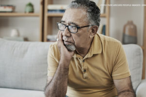 Imagem Acessível: A imagem mostra um homem idoso sentado em um sofá, com uma expressão de preocupação. Ele está usando óculos e uma camisa polo amarela. Ele apoia o rosto em uma das mãos, com o olhar voltado para o lado, parecendo pensativo. Ao fundo, há uma estante com alguns objetos de decoração e livros, sugerindo um ambiente doméstico. Conteúdo textual: “Jabuti” - Reforma da previdência para servidores estaduais e municipais é escamoteada na PEC 66/2023.