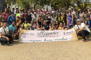 A imagem mostra os filiados e os diretores do SINJUS-MG posando juntos ao ar livre, em um ambiente cercado por vegetação. Elas estão em frente a uma placa que diz 33º Passeio Ecológico, Agosto 2024, Sejam bem-vindos SINJUS MG. As pessoas estão sorrindo e algumas usam óculos de sol e chapéus.