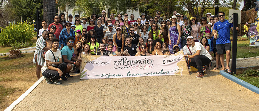 A imagem mostra os filiados e os diretores do SINJUS-MG posando juntos ao ar livre, em um ambiente cercado por vegetação. Elas estão em frente a uma placa que diz 33º Passeio Ecológico, Agosto 2024, Sejam bem-vindos SINJUS MG. As pessoas estão sorrindo e algumas usam óculos de sol e chapéus.