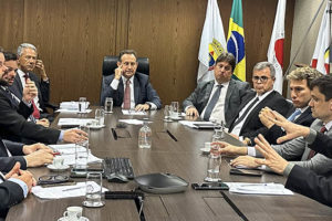 Imagem acessível: Imagem da sala de reuniões, onde há a mesa de negociações, se vê na imagem a Administração do Órgão e os três sindicatos, SINJUS, SERJUSMIG e SINDOJUS, sentados ao redor dela, entre eles o presidente do TJMG o desembargador Luiz Carlos de Azevedo Corrêa Júnior, o coordenador geral do SINJUS Alexandre Pires, na imagem, o mesmo está gesticulando enquanto está falando, ao lado esquerdo da mesa se vê o diretor de assuntos jurídicos do SINJUS Felipe Rodrigues