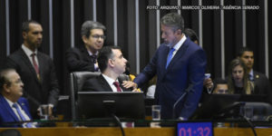 As imagens retratam uma reunião formal no ambiente legislativo brasileiro, com foco na aprovação do Propag. Nelas, há dois homens em destaque, ambos de terno, com um deles tocando o ombro do outro. O fundo apresenta outras pessoas, com uma atmosfera de debate