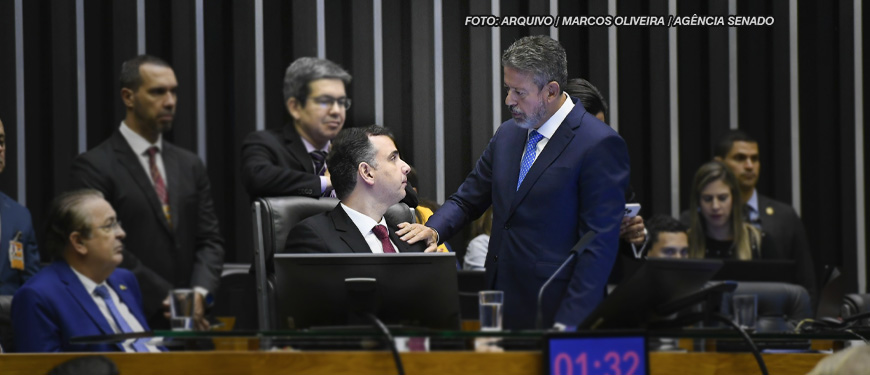 As imagens retratam uma reunião formal no ambiente legislativo brasileiro, com foco na aprovação do Propag. Nelas, há dois homens em destaque, ambos de terno, com um deles tocando o ombro do outro. O fundo apresenta outras pessoas, com uma atmosfera de debate