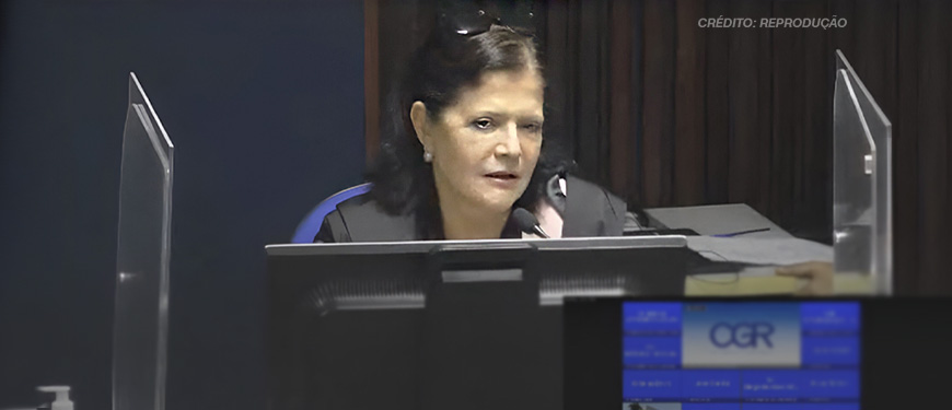 A imagem mostra a desembargadora Rosita Falcão sentada em um ambiente formal, com microfone à sua frente e um monitor em destaque. Ela tem cabelos pretos e usa um traje formal preto. No contexto, há o título: "Fenajud repudia declarações racistas da desembargadora Rosita Falcão sobre cotas raciais", destacando uma nota pública de repúdio sobre comentários racistas.