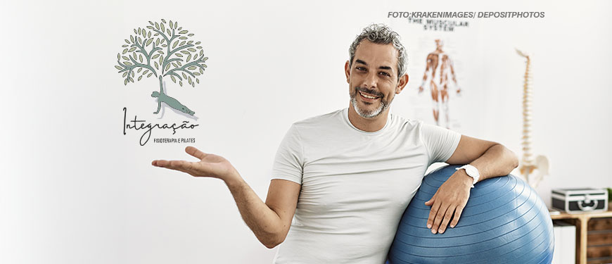 Homem de cabelos grisalhos, barba curta, usando uma camiseta branca e calça preta, está sentado ao lado de uma bola de pilates azul. Ele está sorrindo e com uma das mãos estendida em um gesto amigável. Ao fundo, há uma imagem anatômica de um corpo humano e o logotipo da "Integração Fisioterapia e Pilates", que mostra uma árvore com um tronco estilizado como uma pessoa fazendo uma postura de yoga.