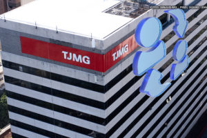 A imagem mostra a lateral de um prédio com a marca "TJMG" em letras brancas sobre uma faixa vermelha, que é o Tribunal de Justiça de Minas Gerais. A foto é tirada de um ângulo que destaca as linhas horizontais do edifício. Sobre a imagem do prédio, há ícones azuis brilhantes que representam pessoas e setas em um círculo, simbolizando troca.