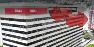 Edifício do Tribunal de Justiça de Minas Gerais (TJMG), com a fachada destacando duas áreas em vermelho na parte superior, onde está o logotipo do TJMG em placas visíveis. O edifício está localizado em uma área urbana com outros prédios ao redor