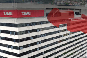 Edifício do Tribunal de Justiça de Minas Gerais (TJMG), com a fachada destacando duas áreas em vermelho na parte superior, onde está o logotipo do TJMG em placas visíveis. O edifício está localizado em uma área urbana com outros prédios ao redor